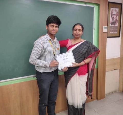 Karthikeya with his teacher, holding the merit certificate